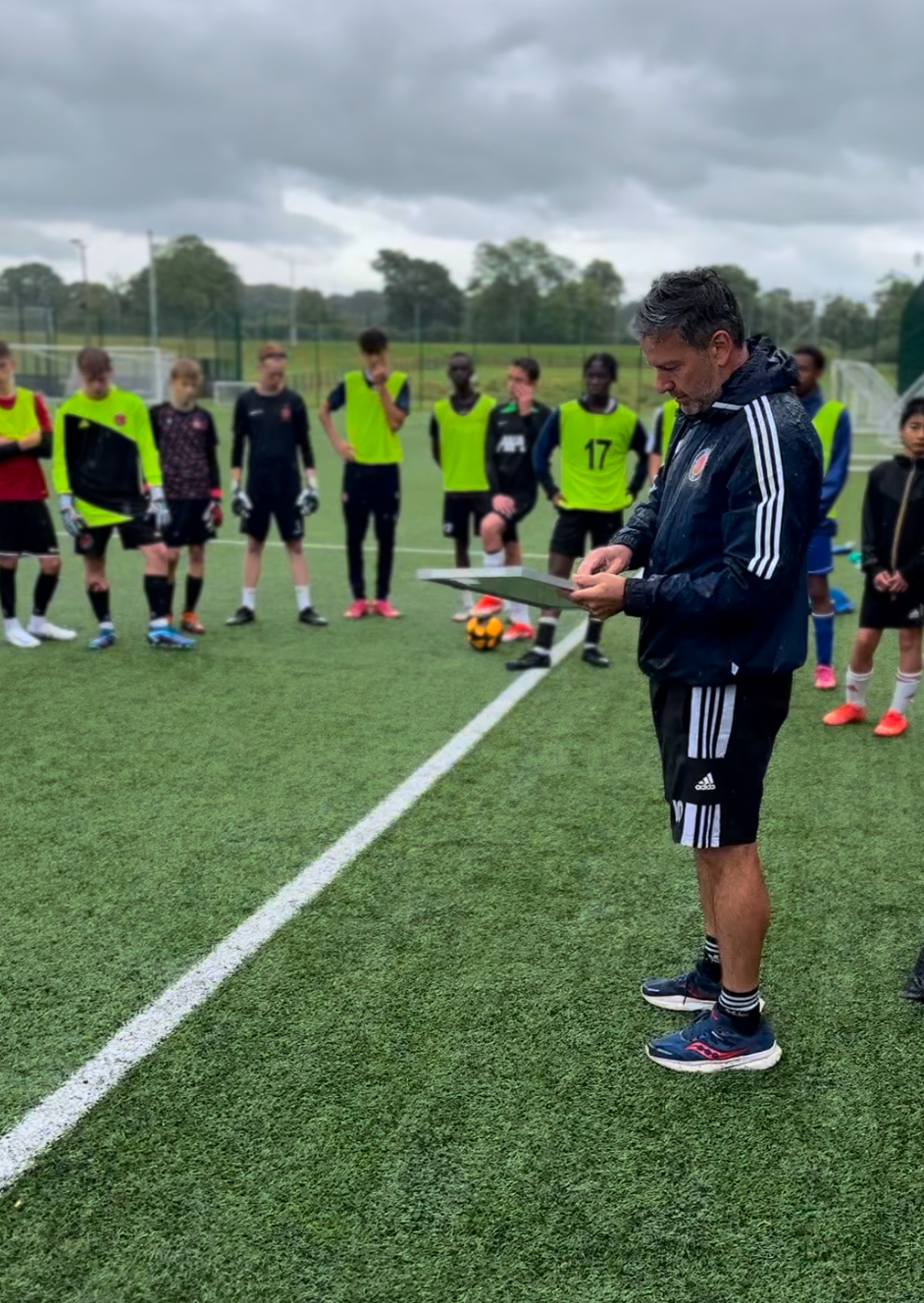 A UEFA qualified IOF Football Coach leading a training session with young players at a soccer academy.